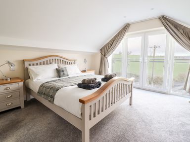 A bedroom with a double bed two bedside tables lamps and curtains by glass doors at Hen Dy Bryn Mawndy Melin y Wig near Corwen
