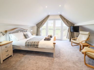 A bedroom with a double bed bedside tables armchairs and a wall-mounted TV at Hen Dy Bryn Mawndy Melin y Wig near Corwen