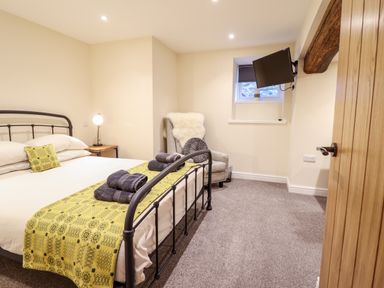 A bedroom with a metal bed frame a bedside table with lamp an armchair with cushions a wall mounted television and a window at Hen Dy Bryn Mawndy in Melin y Wig near Corwen