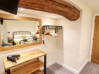 A bedroom corner with a wooden beam a mirror wooden shelves with a hairdryer wall-mounted clothes rack with hangers and a wooden door at Hen Dy Bryn Mawndy Melin y Wig near Corwen
