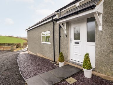 The exterior front entrance of a house with a white door and two potted plants at Hen Dy Bryn Mawndy Melin y Wig near Corwen