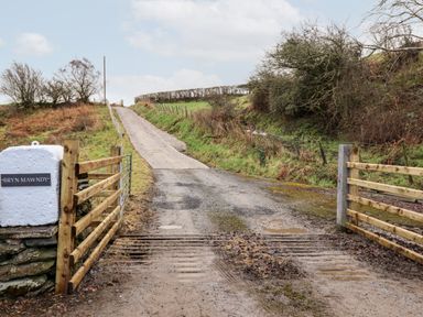 A country road with wooden gates and a sign reading Bryn Mawndy at Hen Dy Bryn Mawndy Melin y Wig near Corwen