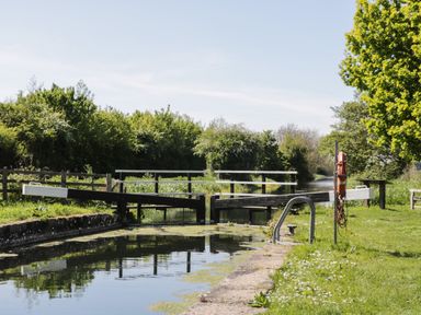 A canal lock with wooden gates surrounded by greenery and a lifebuoy on a post at Robins Nest Cottage in Brandesburton