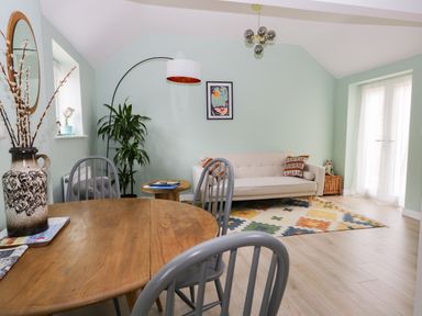 A living room with a wooden table and chairs a beige sofa colorful rug and a tall plant at Robins Nest Cottage in Brandesburton