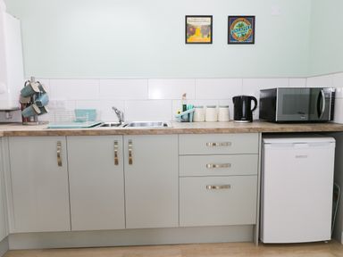 A kitchen counter with a sink dish rack mugs kettle microwave and small refrigerator at Robins Nest Cottage in Brandesburton