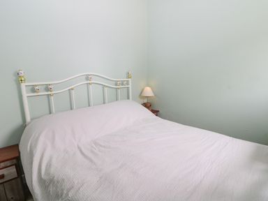 A bedroom with a white metal bed frame a white bedspread a bedside table with a lamp at Robins Nest Cottage in Brandesburton