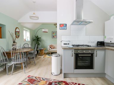 A kitchen with stove and dining area with wooden table and chairs and small sitting area at Robins Nest Cottage in Brandesburton