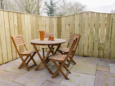 An outdoor patio area with a wooden round table and four wooden chairs with a wooden fence surrounding the space at Robins Nest Cottage in Brandesburton