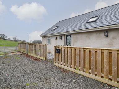 A gravel driveway with a wooden fence and gate in front of a house with a gray slate roof at 3 Mountain View in Talwrn near Llangefni