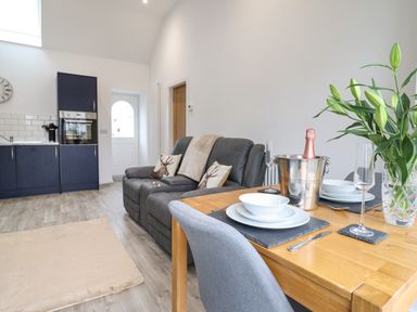 A kitchen and living area with a sofa and dining table set with dishes and a champagne bottle at 3 Mountain View in Talwrn near Llangefni