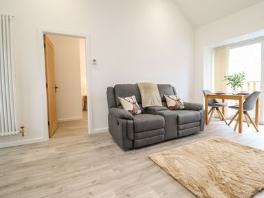 A living room with a gray sofa and two deer pillows a wooden dining table with chairs and a beige rug at 3 Mountain View in Talwrn near Llangefni