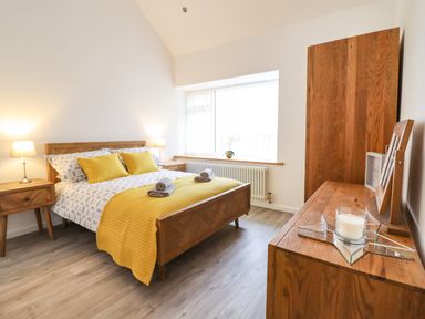 A bedroom with a wooden bed, two bedside tables with lamps, a wooden wardrobe, and a dresser with a candle at 3 Mountain View in Talwrn near Llangefni