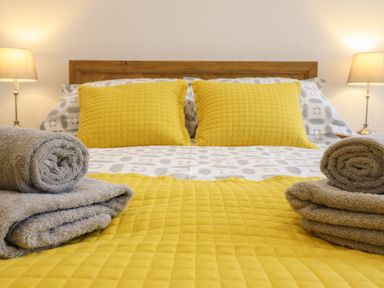A bed with yellow pillows and a yellow quilt with folded gray towels on the sides at 3 Mountain View in Talwrn near Llangefni
