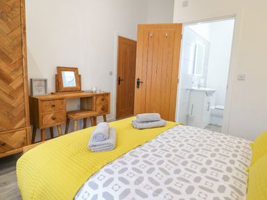 A bedroom with a yellow bedspread two rolled towels on the bed wooden dresser and wardrobe with a door leading to a bathroom at 3 Mountain View in Talwrn near Llangefni