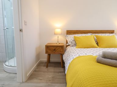 A bedroom with a wooden bed and nightstand with a lamp next to a bathroom at 3 Mountain View in Talwrn near Llangefni
