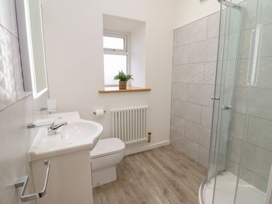 A bathroom with a sink toilet radiator shower and a window with a plant on the sill at 3 Mountain View in Talwrn near Llangefni