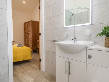A bathroom with a sink and cabinet looking into a bedroom with a yellow bedspread at 3 Mountain View in Talwrn near Llangefni