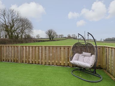 An outdoor area with artificial grass a wooden fence and a hanging wicker chair at 3 Mountain View in Talwrn near Llangefni