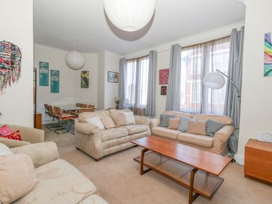 A living room with beige sofas a wooden coffee table and large windows at Victorian Town House in Weymouth