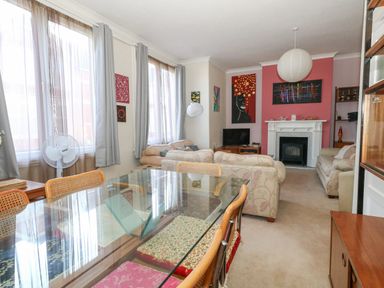 A living room with sofas dining table glass top and paintings on the wall at Victorian Town House in Weymouth