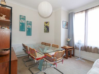 A dining room with a glass table and six chairs next to a window with curtains and a standing fan Victorian Town House Weymouth