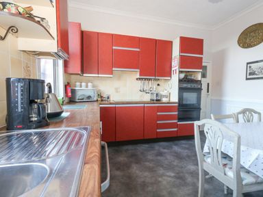 A kitchen with red cabinets a wooden countertop a coffee maker a kettle a toaster and a dining table with chairs at Victorian Town House Weymouth