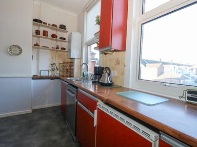 A kitchen with red cabinets a window a toaster kettle coffee maker and shelves with pots at Victorian Town House in Weymouth