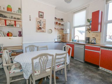 A kitchen with a dining table and six chairs next to red cabinets and shelves at Victorian Town House in Weymouth