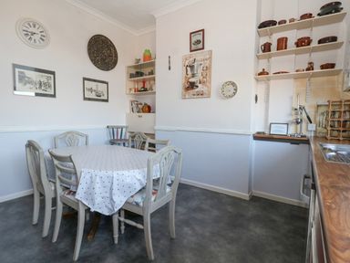 A kitchen dining area with a round table covered by a tablecloth and six chairs at Victorian Town House Weymouth