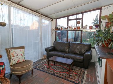 A seating area with a leather sofa wooden coffee table patterned rug armchair with floral cushion potted plants on windowsill at Victorian Town House in Weymouth