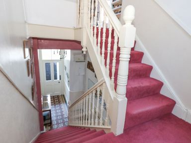 A staircase with red carpet and white balusters next to a hallway with patterned tile floor at Victorian Town House in Weymouth
