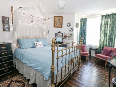 A bedroom with a brass bed frame blue bedding two pink chairs by a window with green curtains at Victorian Town House in Weymouth