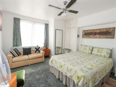 A bedroom with a bed with butterfly bedding a sofa with cushions a ceiling fan and a full length mirror at Victorian Town House in Weymouth