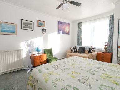 A bedroom with a bed covered in a butterfly patterned duvet a beige sofa with cushions two wooden bedside tables a green chair a standing fan a globe and framed pictures on the wall at Victorian Town House in Weymouth