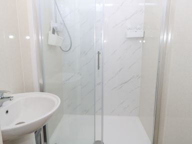 A bathroom with a white sink and a glass enclosed shower with a marble patterned wall at Victorian Town House in Weymouth