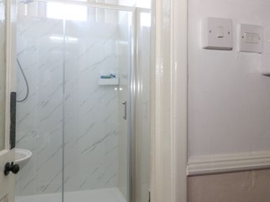 A shower with glass doors and marble patterned walls in a bathroom at Victorian Town House in Weymouth