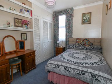 A bedroom with a double bed a wooden dressing table with a stool built in wardrobes and floral curtains at Victorian Town House Weymouth