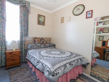 A bedroom with a bed near a window beside a wooden nightstand and a large mirror at Victorian Town House in Weymouth