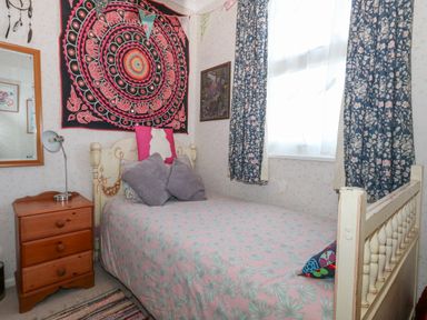 A bedroom with a single bed covered with patterned bedding next to a wooden nightstand with a lamp and a large colorful tapestry on the wall at Victorian Town House in Weymouth