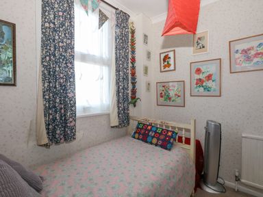 A small bedroom with a single bed under a window with floral curtains and framed floral paintings on the walls at Victorian Town House in Weymouth