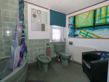 A bathroom with a bathtub bidet and toilet a window a black chair and abstract paintings at Victorian Town House Weymouth