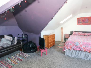 A bedroom with a bed a dresser a black leather sofa and a small TV on a pink table at Victorian Town House in Weymouth