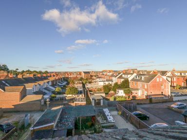 A neighborhood with rows of houses a few cars and gardens under a blue sky at Victorian Town House Weymouth