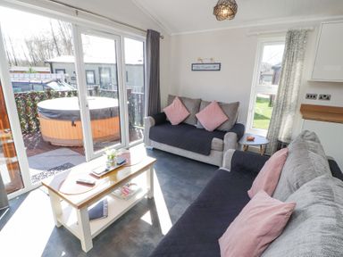 A living room with two sofas a coffee table and sliding glass doors leading to a patio with a hot tub at Duckling Lodge in South Lakeland Leisure Village