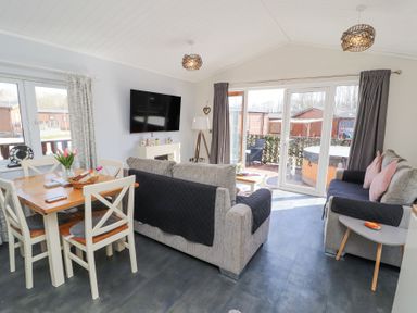 A living room with sofas a dining table a wall mounted television and glass doors leading outside at Duckling Lodge in South Lakeland Leisure Village
