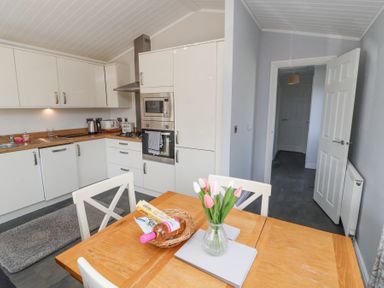 A kitchen with white cabinets wooden countertops a wooden dining table with tulips in a vase and snacks at Duckling Lodge in South Lakeland Leisure Village