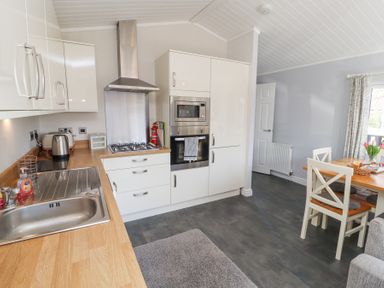 A kitchen with countertop sink gas stove oven microwave dining table and chairs at Duckling Lodge in South Lakeland Leisure Village