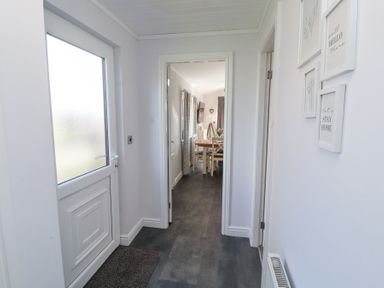 A hallway with a white door and a mat leading to a dining area with a table and chairs at Duckling Lodge South Lakeland Leisure Village