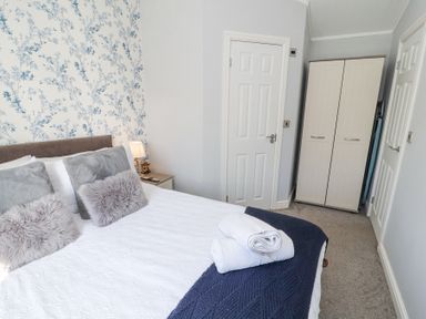 A bedroom with a bed with pillows and towels a nightstand with a lamp a wardrobe and two doors at Duckling Lodge South Lakeland Leisure Village