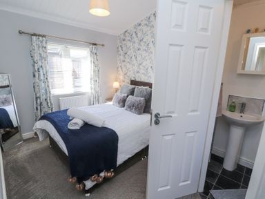 A bedroom with a bed and pillows a window with curtains and an en suite bathroom at Duckling Lodge in South Lakeland Leisure Village